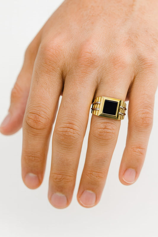 Gold ring with a black stone on a person's finger against a white background